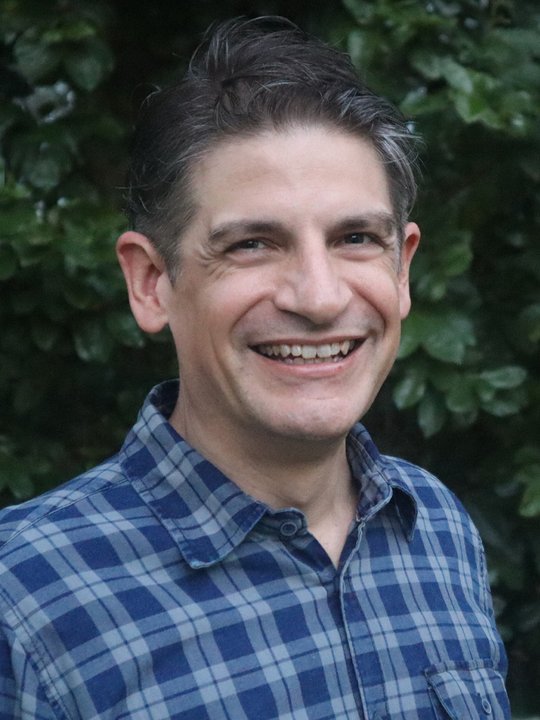 Portrait of Jason Betler, smiling, in a blue plaid shirt.